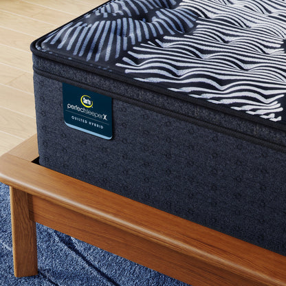 Corner of Perfect Sleeper X Quilted Hybrid Max Firm Pillow Top Mattress sitting in a brown bedframe || feel: Firm Pillow Top || level: Level 2