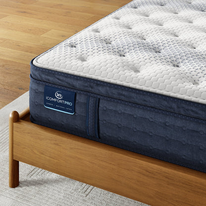 Corner of iComfortPro Dartmouth Pillow Top Mattress sitting in a brown bedframe || feel: plush pillow top || level: Level 2