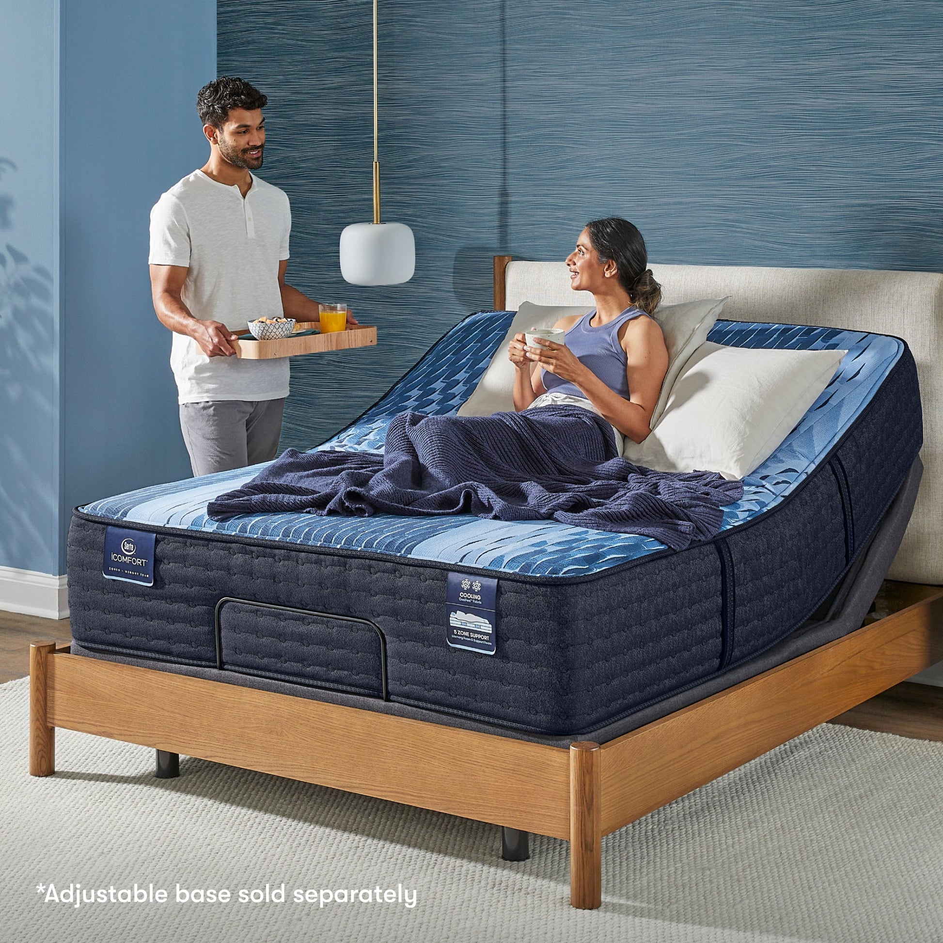 Woman siting in a slightly bent Serta iComfort mattress placed on an adjustable base looking at a man standing at the side serving breakfast in bed || feel: plush || level: Enhanced - 14"