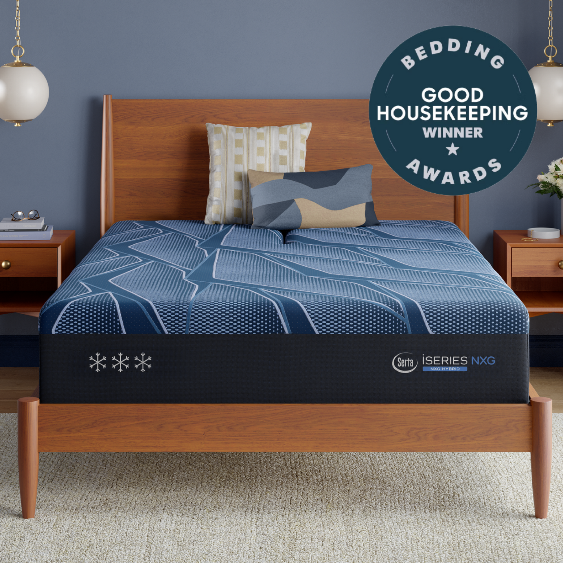 A Blue Serta® iSeries® NXG™ Mattress on a wooden bed frame in a styled bedroom setting, with blue patterned bedding, matching pillows, bedside tables, pendant lights, and a circular 'Bedding Good Housekeeping Winner Awards' badge in the top right.