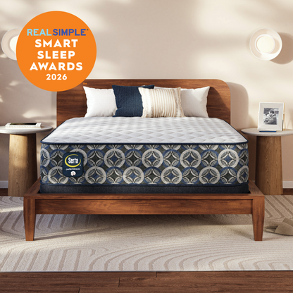 A Serta Perfect Sleeper firm mattress on a wooden bed frame in a styled bedroom setting, with a circular orange 'Real Simple Smart Sleep Awards 2026' badge in the top-left corner.