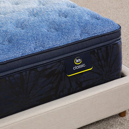 Corner of Serta classic brecon plush pillow top mattress sitting in a beige bed frame ||feel: Plush pillow top ||level: enhanced